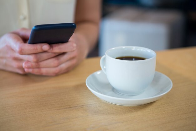 커피 숍에서 테이블에 휴대 전화와 커피 컵을 사용하는 여자