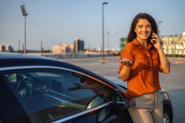 Photo woman using mobile phone communication or online application standing near car on city street or parking outdoors car sharing rental service or taxi app