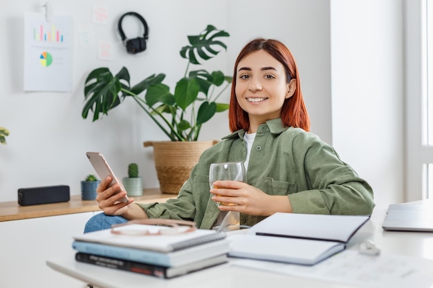 Woman using mobile phone and drinking tea Young businesswoman at comfortable workplace