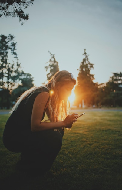 夕暮れの空に向かってフィールドで携帯電話を使っている女性