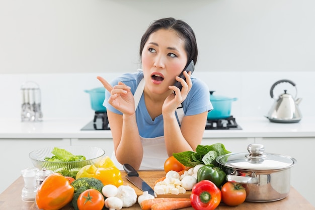 Женщина, используя мобильный телефон перед овощами в кухне