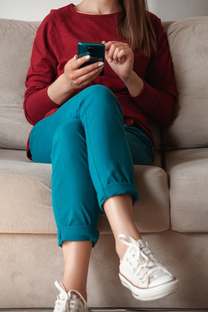 Woman using mobile phone, holding in hands sitting on sofa