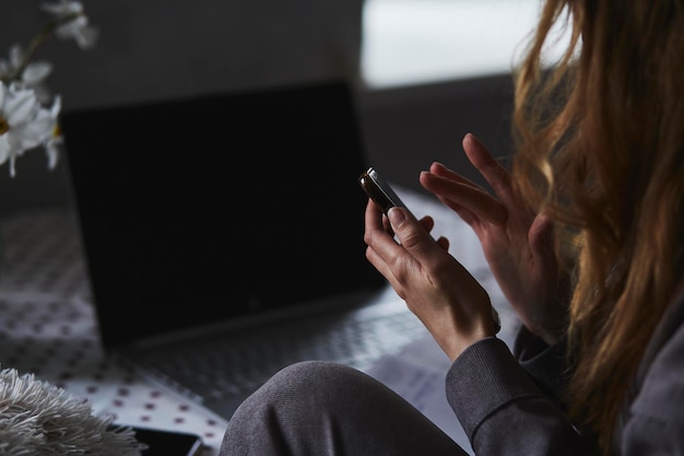 Женщина, использующая мобильный телефон в домашнем офисе с ноутбуком Внештатный, работающий удаленно Новое нормальное явление