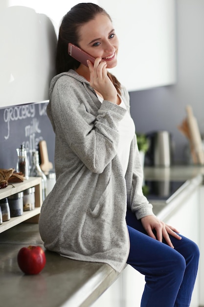 Woman using mobile phone sitting in modern kitchen