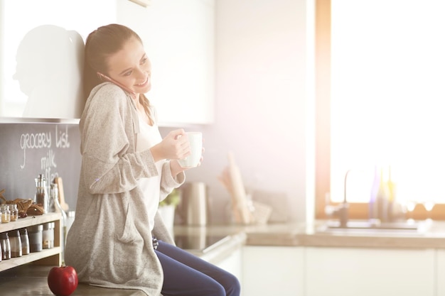 Woman using mobile phone sitting in modern kitchen