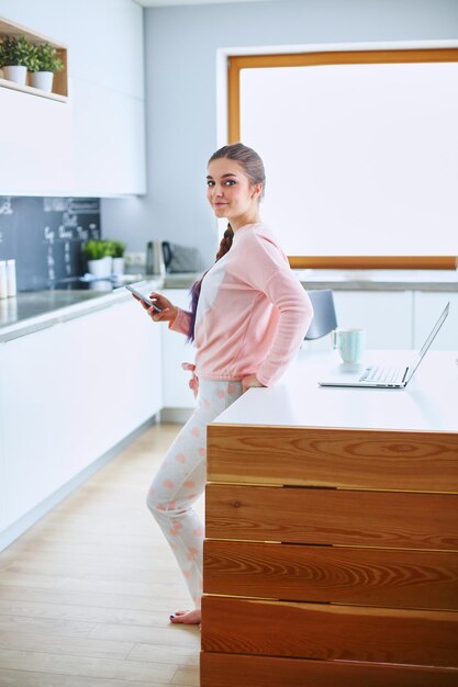 Woman using mobile phone standing in modern kitchen