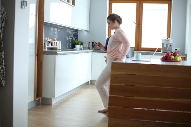 Woman using mobile phone standing in modern kitchen