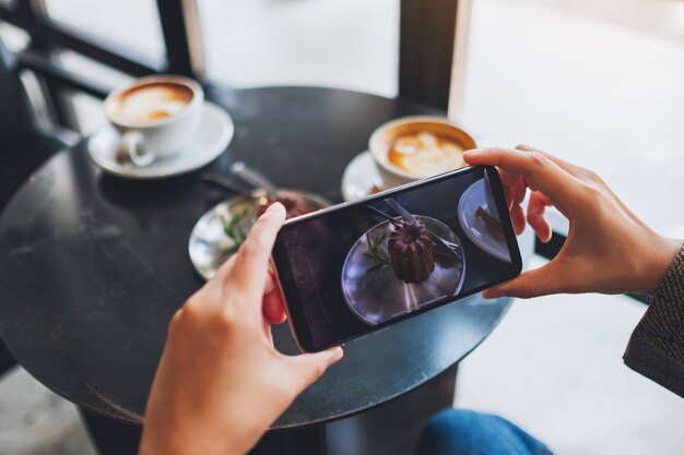 a woman using mobile phone to take a photo of coffee and snack before eat in cafe