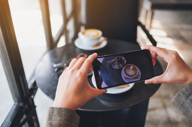 A woman using mobile phone to take a photo of coffee and snack before eat