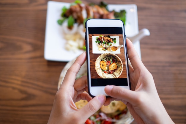 Woman using mobile phone to take pictures of food on the table. Taken on mobile and put on social networks.