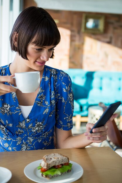 コーヒーを飲みながら携帯電話を使用している女性