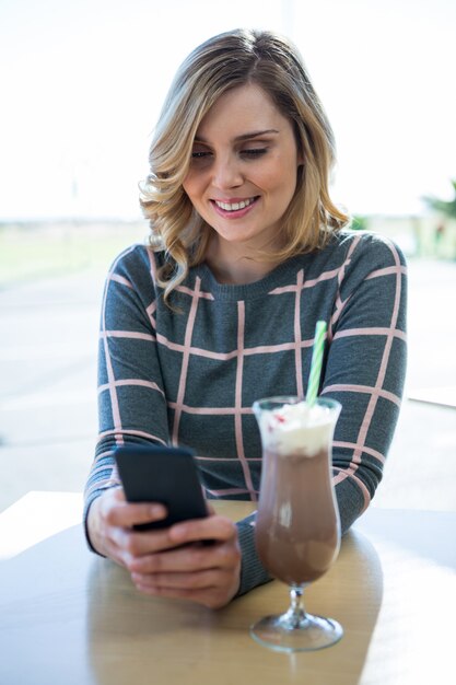 Woman using mobile phone while having milkshake