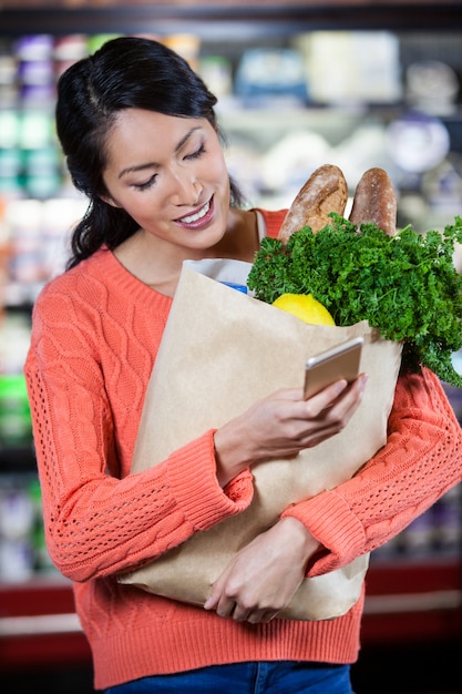 Woman using mobile phone while holding groceries