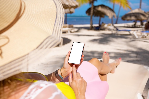 Foto donna che utilizza il telefono cellulare mentre ci si rilassa sulla spiaggia tropicale