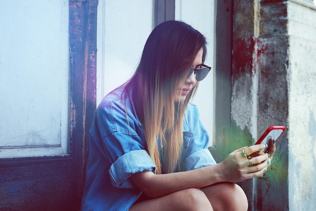 Photo woman using mobile phone while sitting against closed door