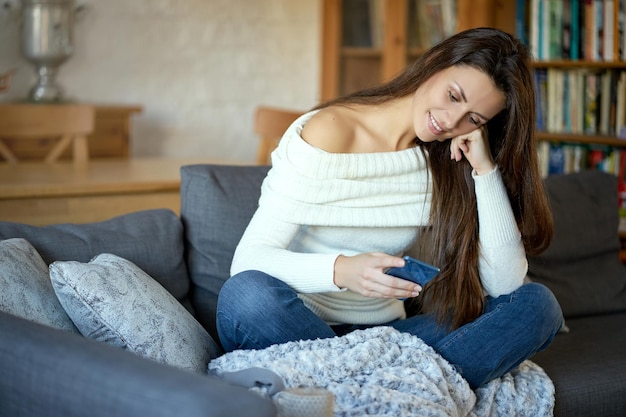 Photo woman using mobile phone while sitting on sofa at home