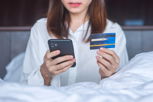가정 기술 전자 상거래 디지털 뱅킹 온라인 지불 및 아파트 생활 개념에서 아침에 침대에서 주문하는 동안 온라인 쇼핑을 위해 모바일 스마트 폰과 신용 카드를 사용하는 여성
