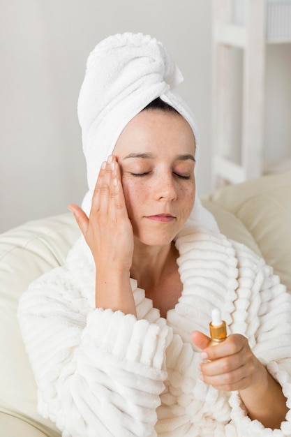 Woman using moisturizer for her skin and wearing a bathrobe