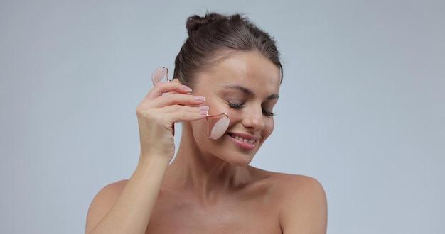 피부 관리 및 스파 미용 치료를 위해 천연 마사지 도구를 사용하는 여성 얼굴 마사지를 위해 옥 페이셜 롤러를 사용하는 어린 소녀 미용 및 피부 관리