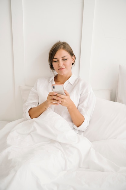 Женщина, использующая телефон на своей белой кровати