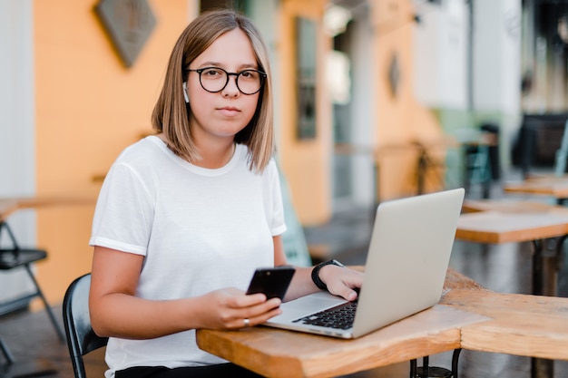 Woman using phone and laptop in the cafe outdoors