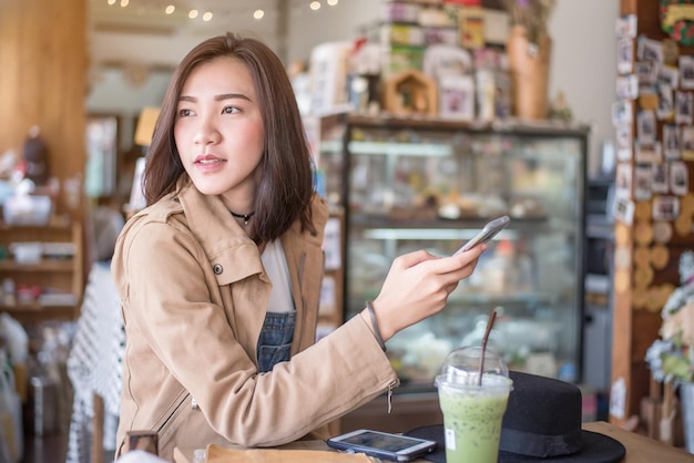 사진 카페 에서 테이블 에 앉아 있는 동안 전화 를 사용하는 여자