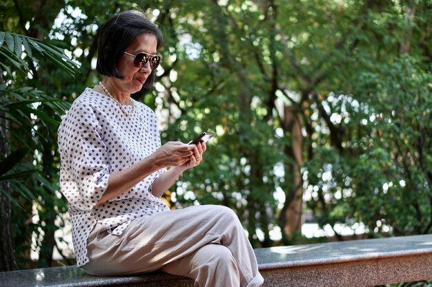 Photo woman using phone while sitting on bench against trees