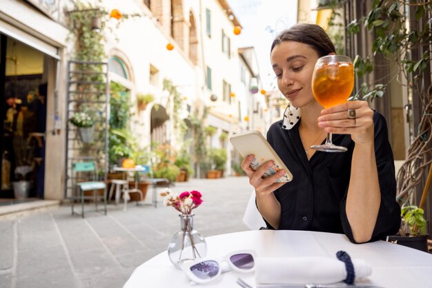 居心地の良い通りにあるイタリアンレストランでワインと一緒に座っている間電話を使用している女性