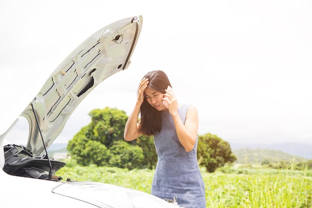 Photo woman using phone while standing by broken down vehicle