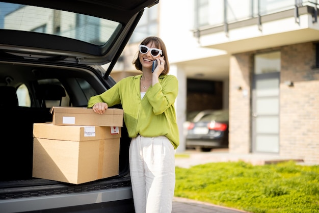 荷物を持って車のトランクの近くに立っているときに電話を使用している女性