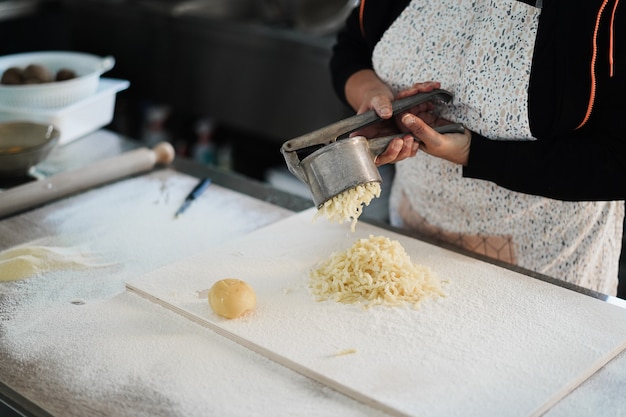 Woman using potato press for fresh hand made gnocchi inside pasta factory