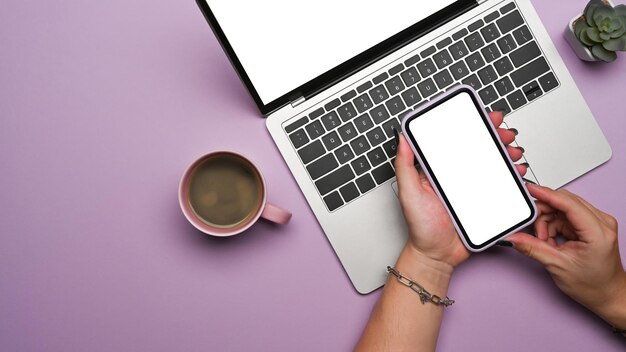 Woman using smart phone and laptop computer on purple background Top view