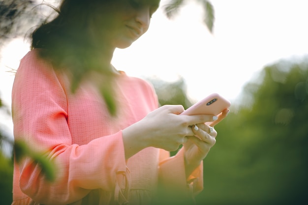 屋外と緑の自然でスマートフォンを使用している女性。スマートフォンを保持している女の子の手