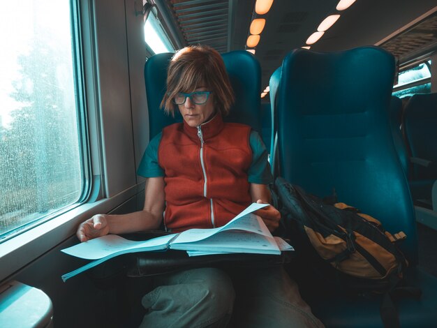 Woman using smart phone sitting traveling by train hand writing on paper. Desaturated cold tone color grading. Working mobility concept. 