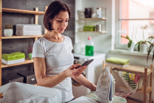 Woman using smart phone while ironing clothes