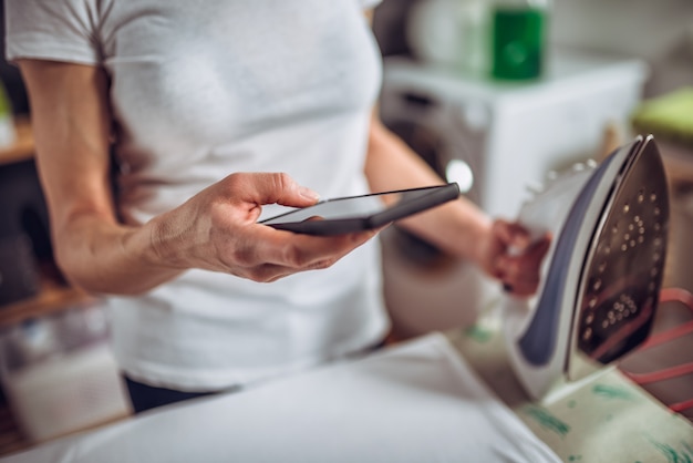 Woman using smart phone while ironing clothes