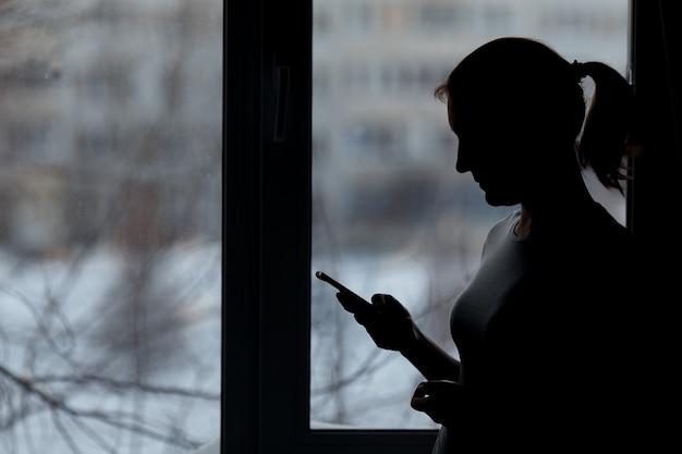 Woman using smart phone at window house background.