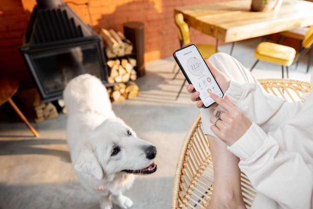 Женщина использует смартфон с запущенным приложением для умного дома дома со своей собакой