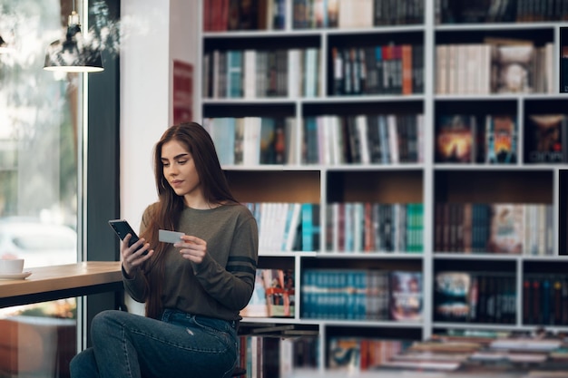 Woman using smartphone and a credit card for online shopping in a cafe