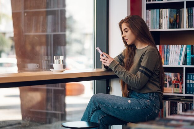 Woman using smartphone and drinking coffee in a cafe