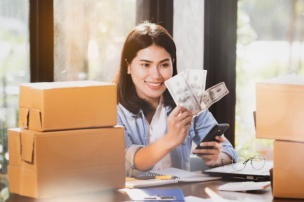 woman using smartphone and holding money banknotes smiles with happy.