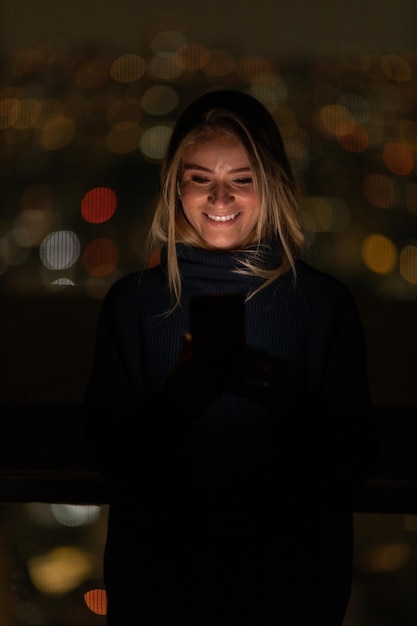 Foto donna che usa uno smartphone di notte con tecnologia di telefono cellulare con vista sulla città e paesaggio