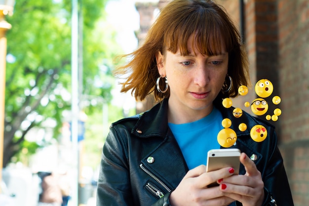 Donna che per mezzo dello smartphone che invia gli emoji.