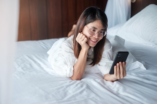 Donna che utilizza smartphone per i social media giovane donna che guarda film dal telefono cellulare sul letto a casa rete tecnologica shopping online e commerce stile di vita e concetto di comunicazione digitale