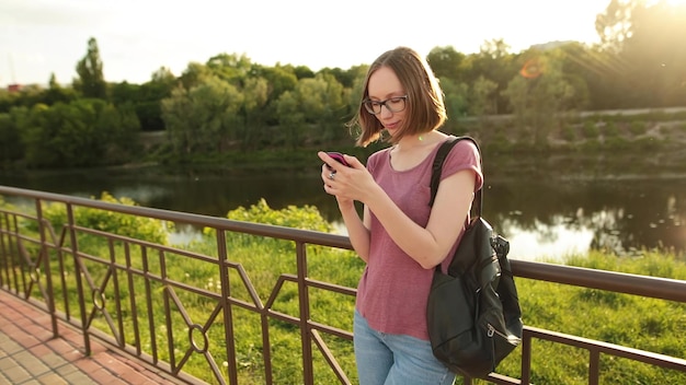 Woman using smartphone standing outdoors on the bridge Hipster girl browsing Internet on a phone texting and communicating