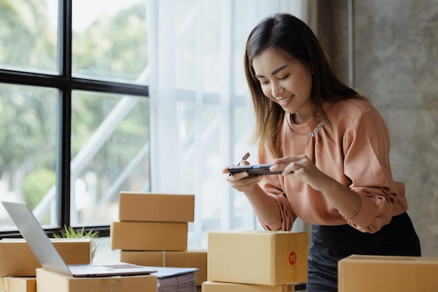 A woman using a smartphone to take pictures in front of parcel boxes parcel boxes for packing goods delivering goods through private courier companies Online selling and online shopping concepts