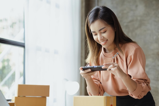 A woman using a smartphone to take pictures in front of parcel\
boxes parcel boxes for packing goods delivering goods through\
private courier companies online selling and online shopping\
concepts