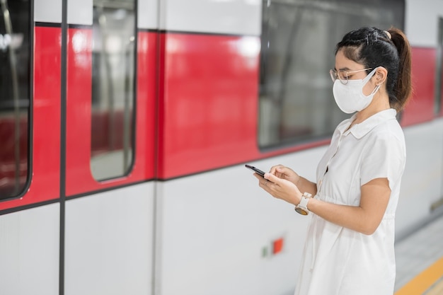 電車の中で保護マスクを着用中にスマートフォンを使用している女性。 covid-19パンデミック下の公共交通機関、技術、安全性