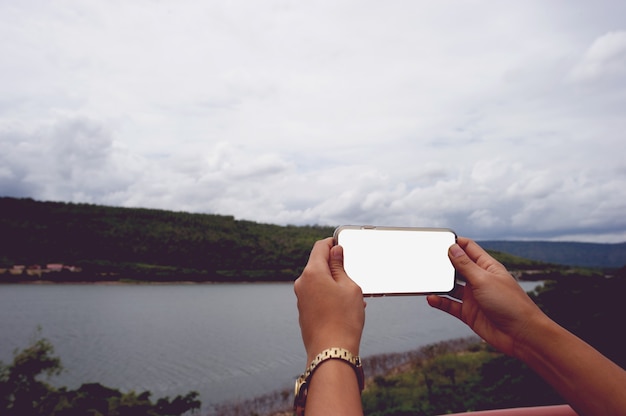 自然の中で空白の画面を持つスマートフォンを使用している女性