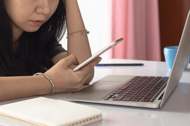 Woman using smartphone with computer laptop and working at home for business, self-quarantine